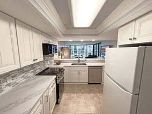A modern kitchen with white cabinetry, a marble countertop, and a built-in stove. - Captains Quarters Oceanfront – Saltwater Sunrises (St. Augustine)