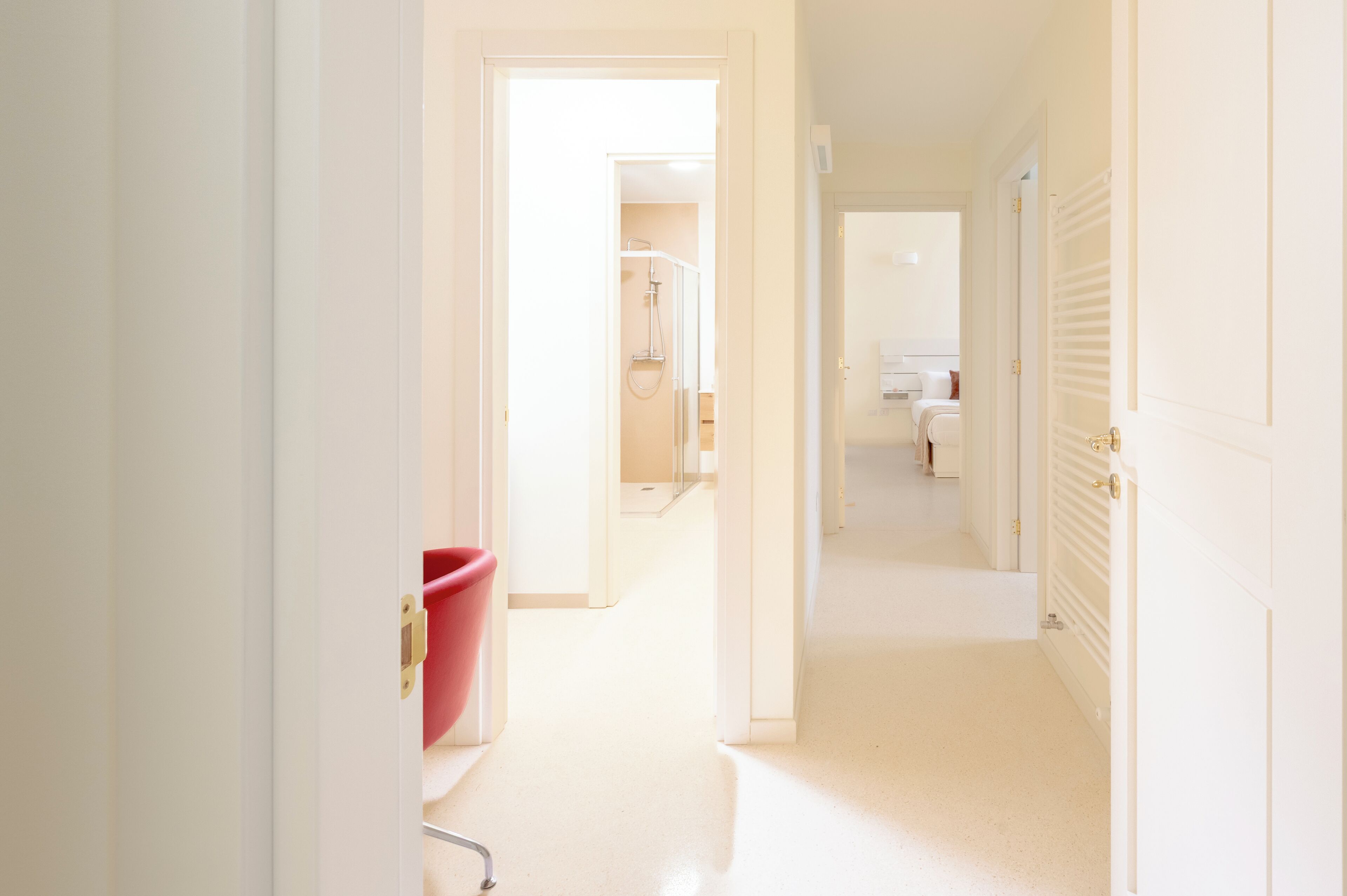 A bright hallway with a red chair, a shower area, and a door leading to a bathroom.