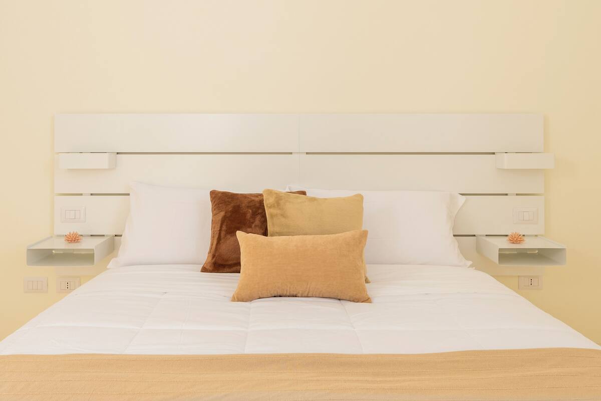 A neatly made bed with a white headboard, two bedside tables with lamps, and a single decorative item on each table.