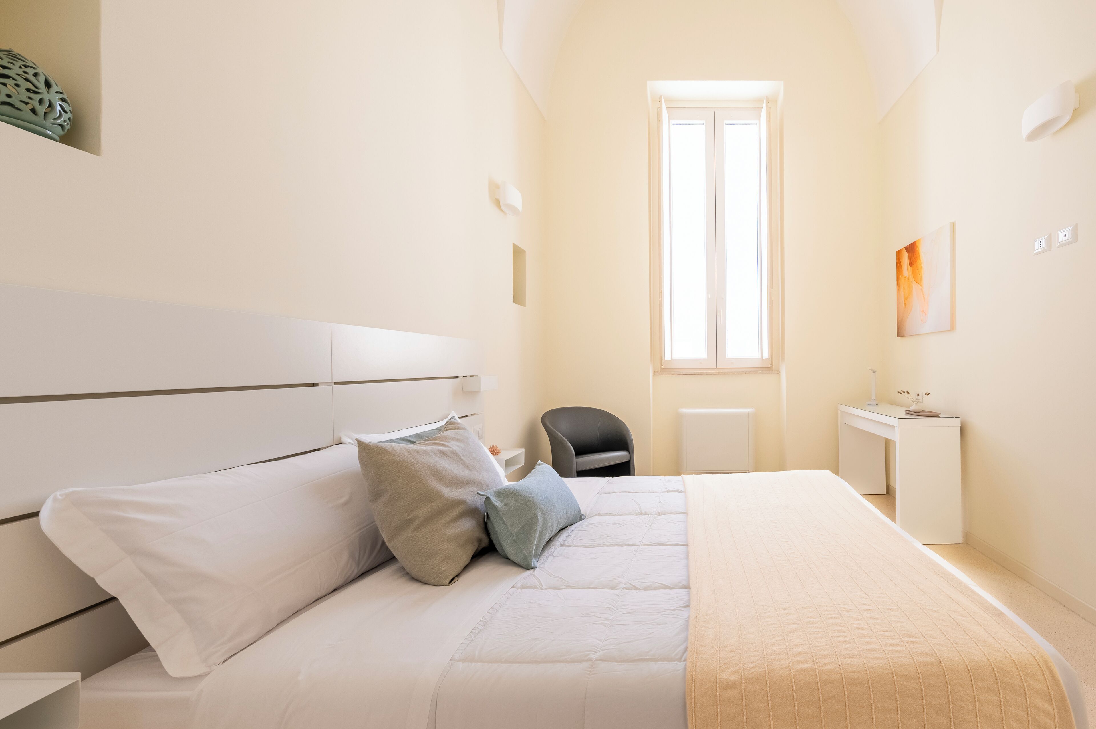 A bedroom with a bed, bedside table, chair, desk, and a window.