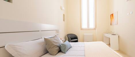 A bedroom with a bed, bedside table, chair, desk, and a window.