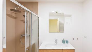 A modern bathroom with a glass-enclosed shower, a white sink with a wooden cabinet, and a mirror above the sink.