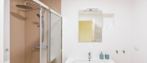 A modern bathroom with a glass-enclosed shower, a white sink with a wooden cabinet, and a mirror above the sink.