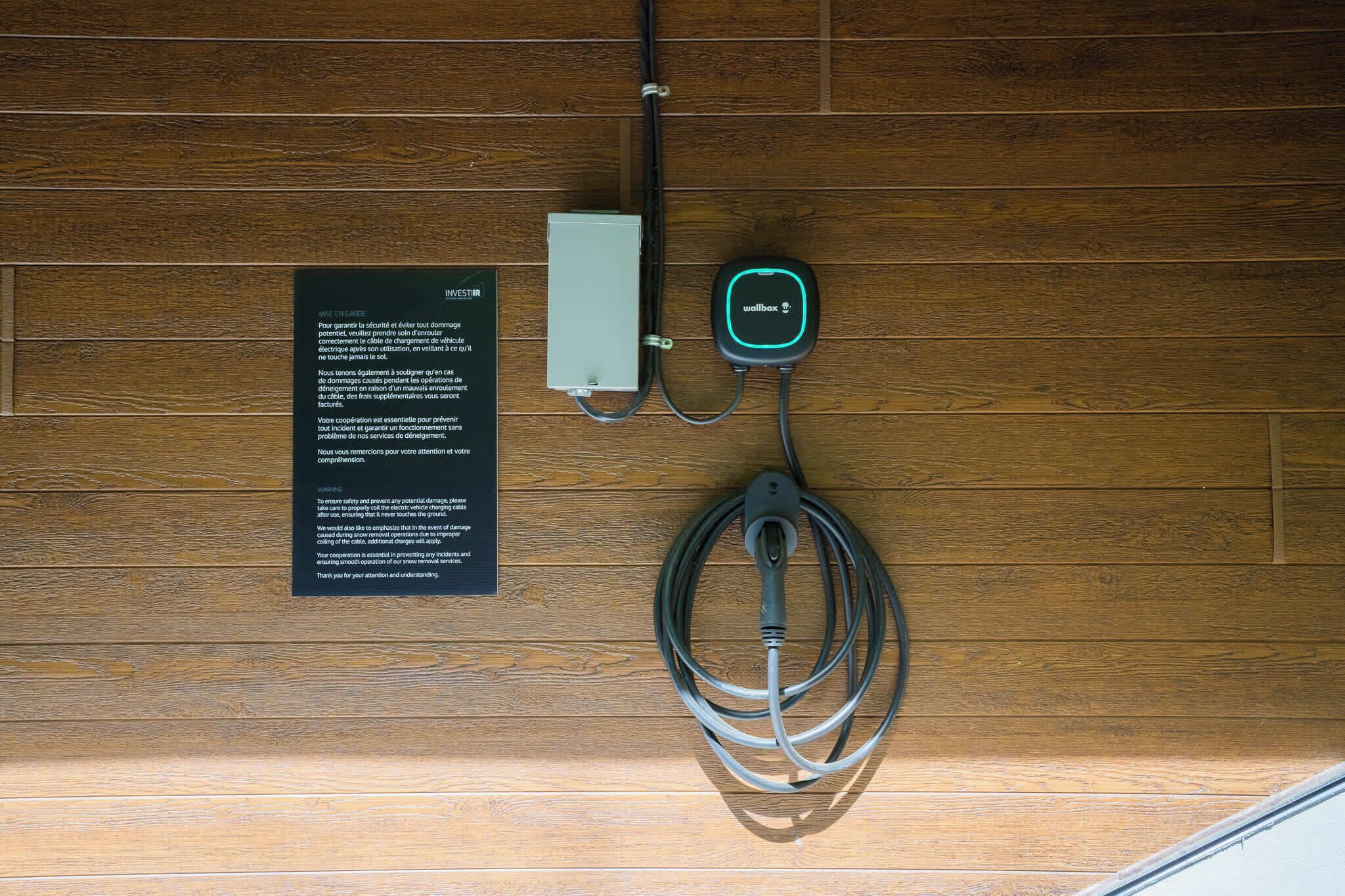 En väggmonterad laddstation med en kabel och en strömkälla, samt en skylt med text.