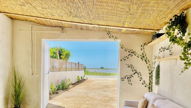 A room with a view of a beach, a thatched roof, a sofa, and a potted plant.