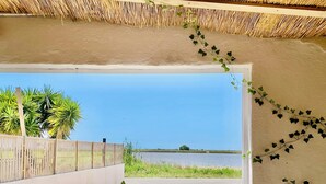 A view from a covered outdoor area to a body of water, with a wooden fence and plants along the side.