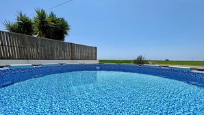 A swimming pool with a blue mosaic tile design, surrounded by a wooden fence and palm trees.