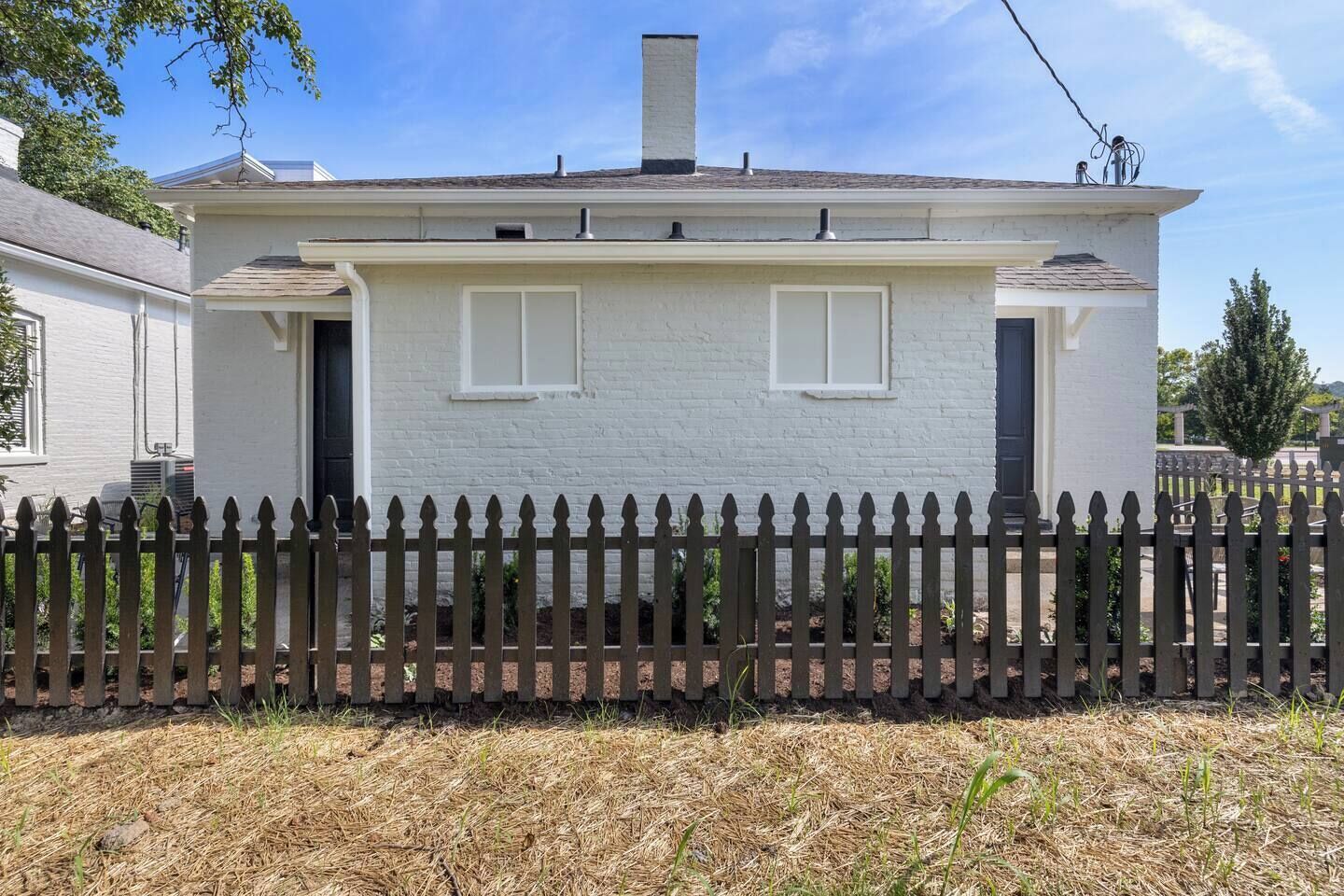 Une maison de plain-pied à l’extérieur blanc, avec une clôture en bois peinte en brun foncé et un ciel dégagé.