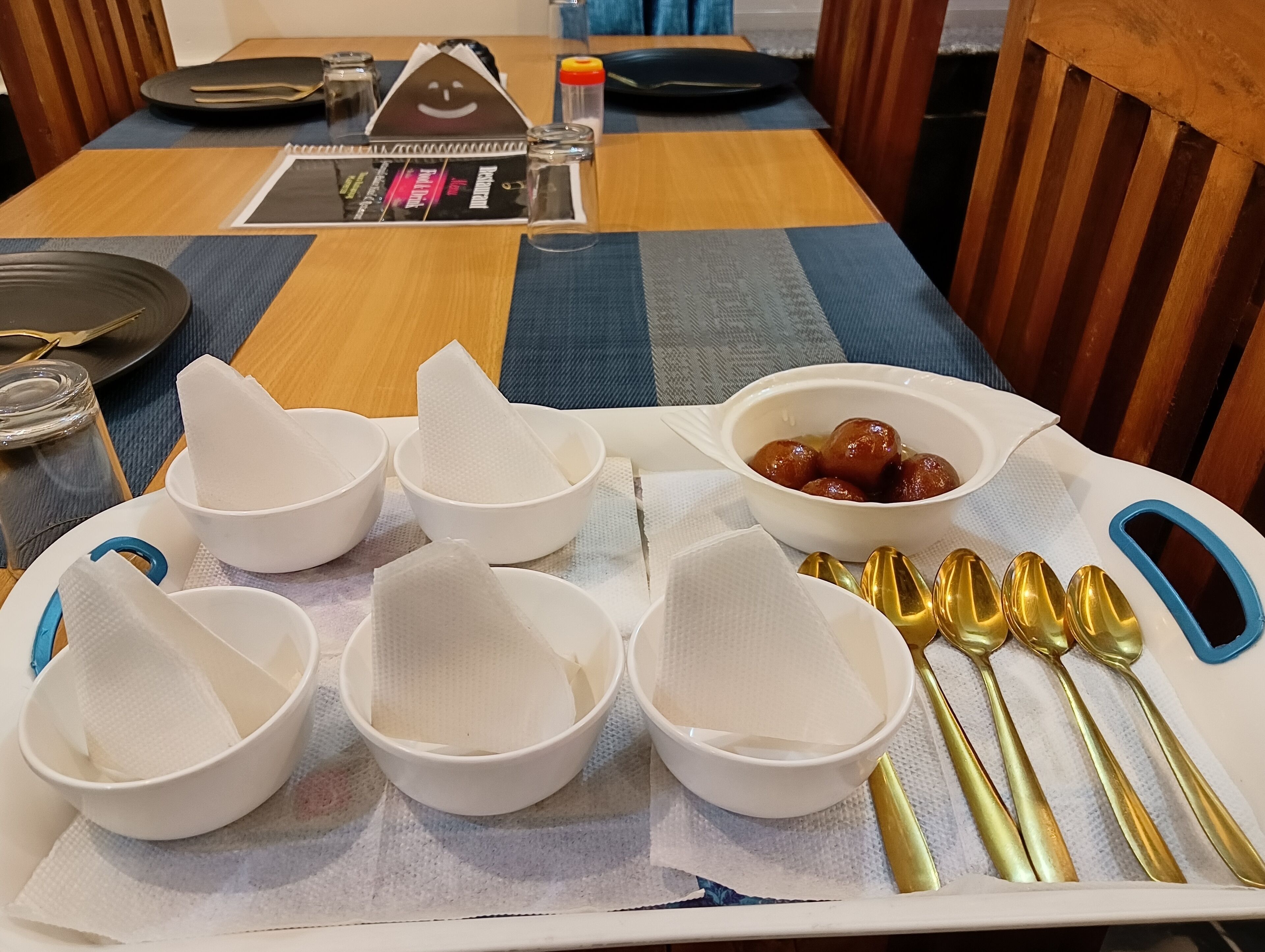 Ein Esstisch ist gedeckt mit weißen Schüsseln, einer Süßigkeitenschale und goldenen Löffeln.