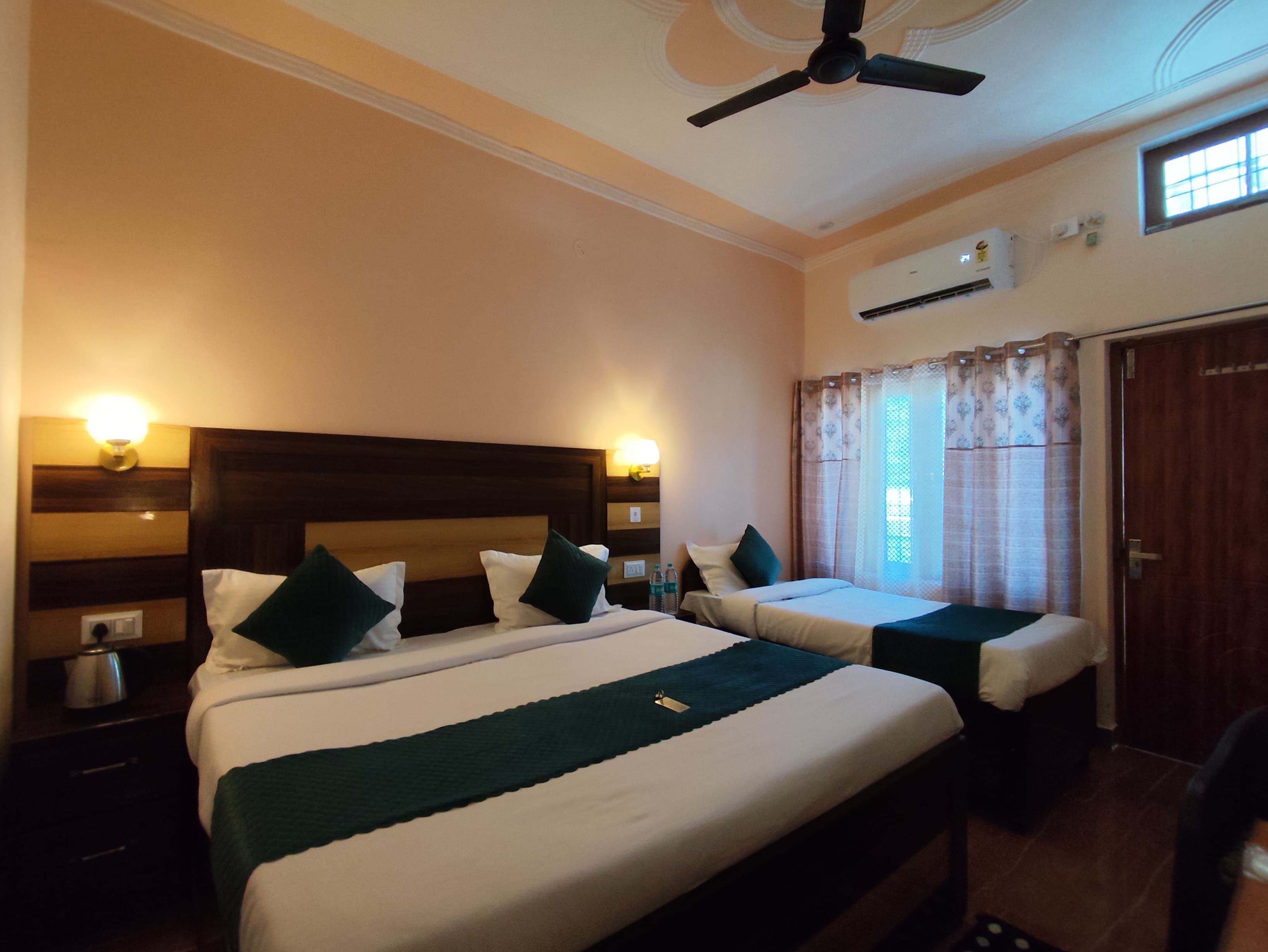 A hotel room with two beds, a ceiling fan, an air conditioning unit, and a window with curtains.