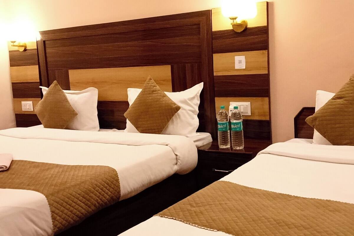 Ein Hotelzimmer mit zwei Betten, jedes mit einem Holz-Kopfteil, weißer Bettwäsche und mehreren Kissen. Auf dem Nachttisch stehen zwei Wasserflaschen.