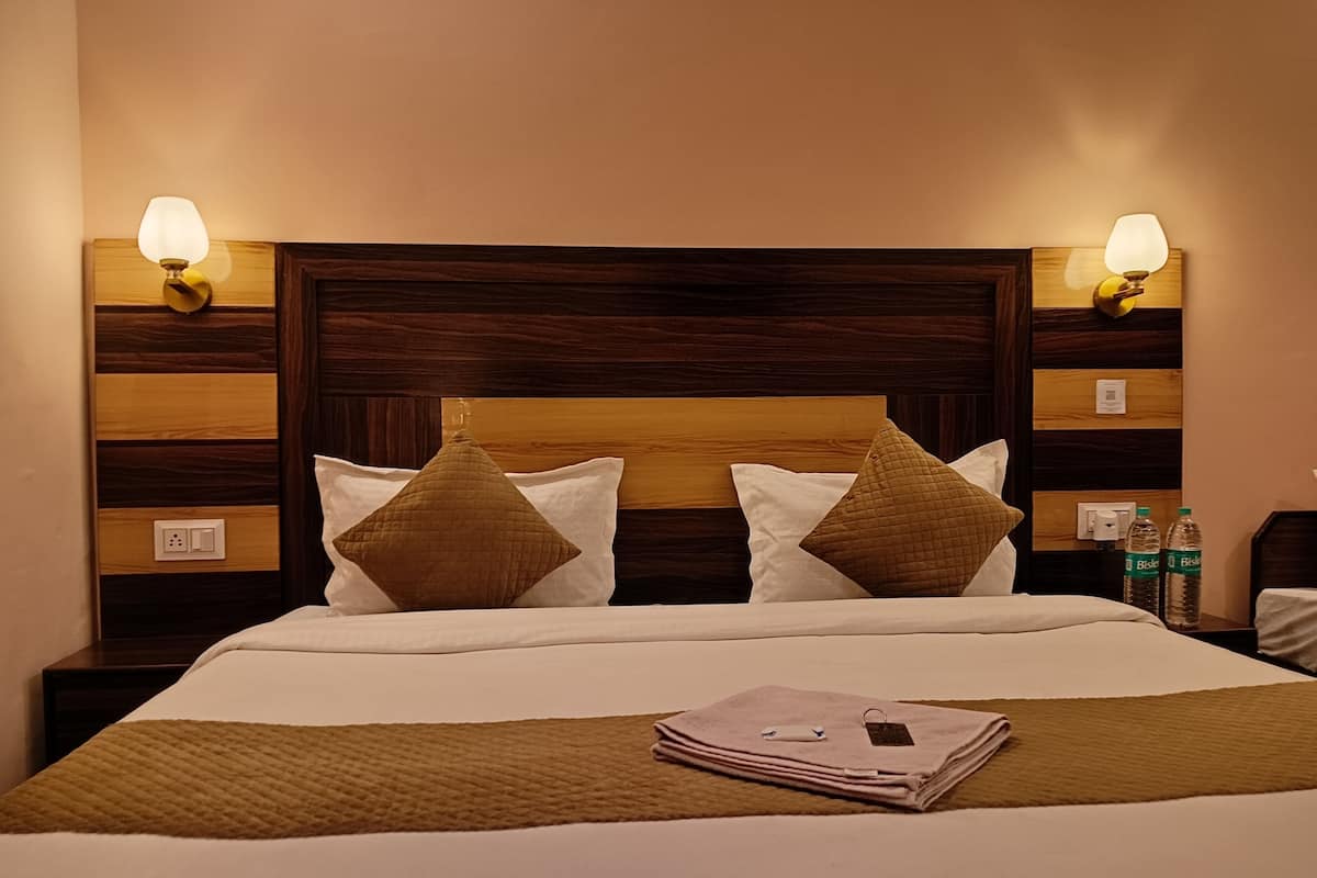 Ein Hotelzimmer mit einem hölzernen Kopfteil, zwei Nachttischlampen, einem Bett mit weißer und brauner Bettwäsche und einem Nachttisch mit einer Wasserflasche.
