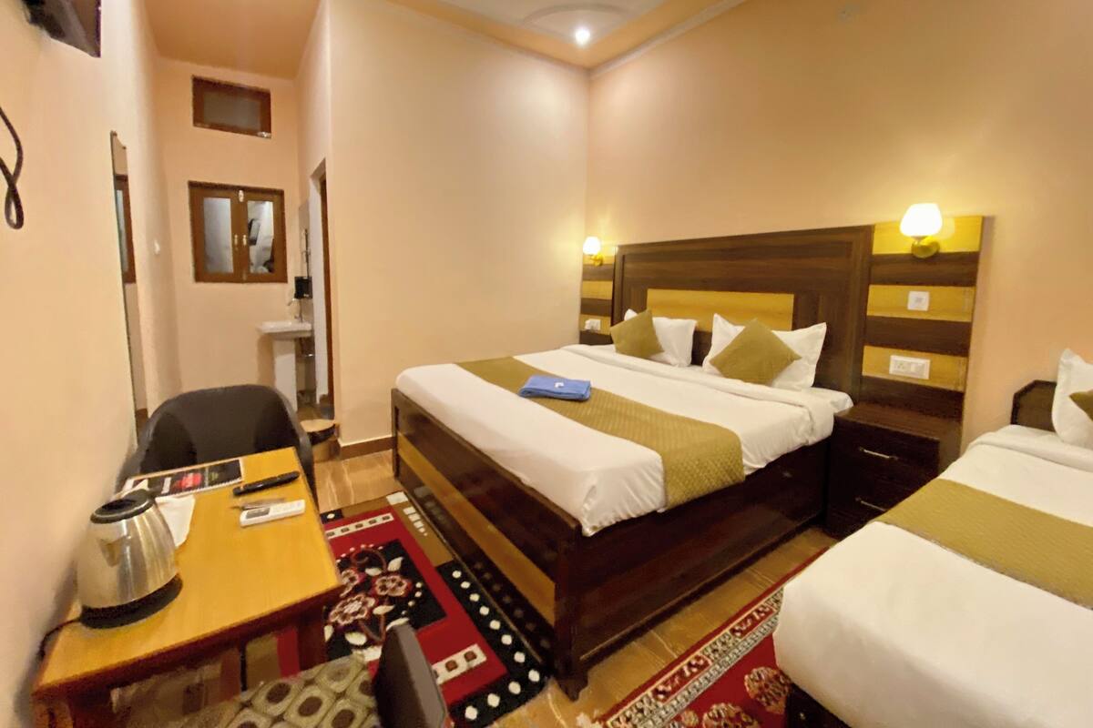 Ein Hotelzimmer mit zwei Einzelbetten, einem Schreibtisch mit Wasserkocher, einem Stuhl und einem gemusterten Teppich.