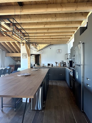 A modern kitchen with a wooden island, stainless steel appliances, and a high ceiling with exposed beams. - Chalet des Lacs Apartment – Alpe d’Huez – Vieil Alpe District (Alpe d'Huez)