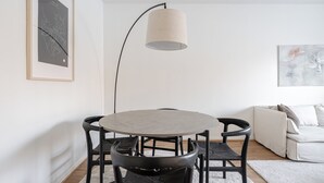 Una sala de estar moderna con una mesa redonda, sillas negras, una lámpara de pie, un sofá y un cuadro abstracto enmarcado.