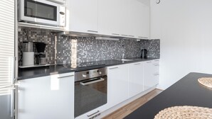 Una cocina moderna con armarios blancos, encimera negra, microondas, cafetera y salpicadero de azulejos.
