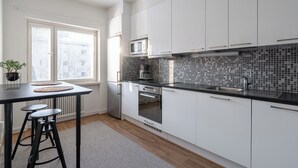 Una cocina moderna con armarios blancos, encimera negra y salpicadero de azulejos. Se aprecia una ventana con persianas, un microondas y un fregadero.