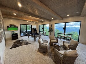 A spacious room with a pool table, comfortable seating, a large window with a mountain view, and a mounted TV.
