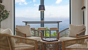 Ein Zimmer mit Korbmöbeln, einem Tisch und Bergblick durch große Fenster.