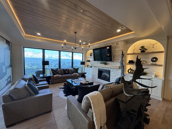 A spacious living room with a fireplace, large windows, and a high ceiling.