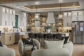 A modern kitchen with white cabinets, a central island, hanging pendant lights, and a stainless steel refrigerator.