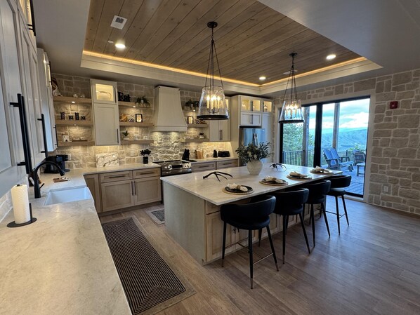A modern kitchen with a large island, pendant lighting, and a view to the outside.