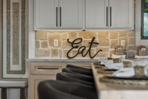 A kitchen with stone backsplash, a wall-mounted 'Eat' sign, and a countertop with various items.