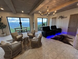A spacious room with wicker furniture, a leather sofa, and a view of mountains through large windows.