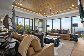 A spacious living room with a large window, a chandelier, and a unique antler sculpture.