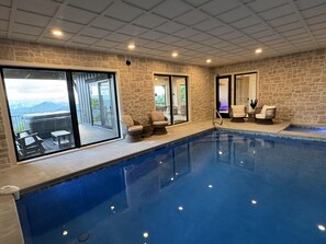 Ein Innenpool mit SteinwĂ€nden und groĂen Fenstern mit Blick auf eine gebirgige Landschaft.
