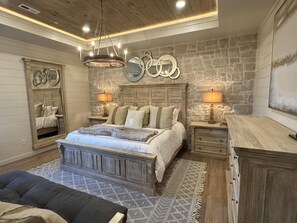 A bedroom with a large bed, two bedside tables with lamps, a dresser, a mirror, and a chandelier.