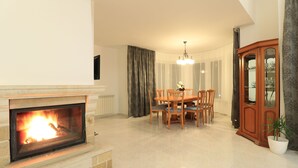 Una sala de estar con chimenea, una mesa de comedor con sillas, una araña y un aparador con puertas de cristal.