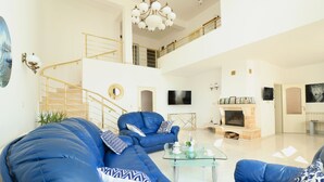 Amplia sala de estar con techo alto, escalera, chimenea y televisor.