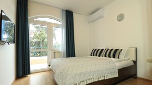 Un dormitorio con cama, televisor, ventana con cortinas y equipo de aire acondicionado.