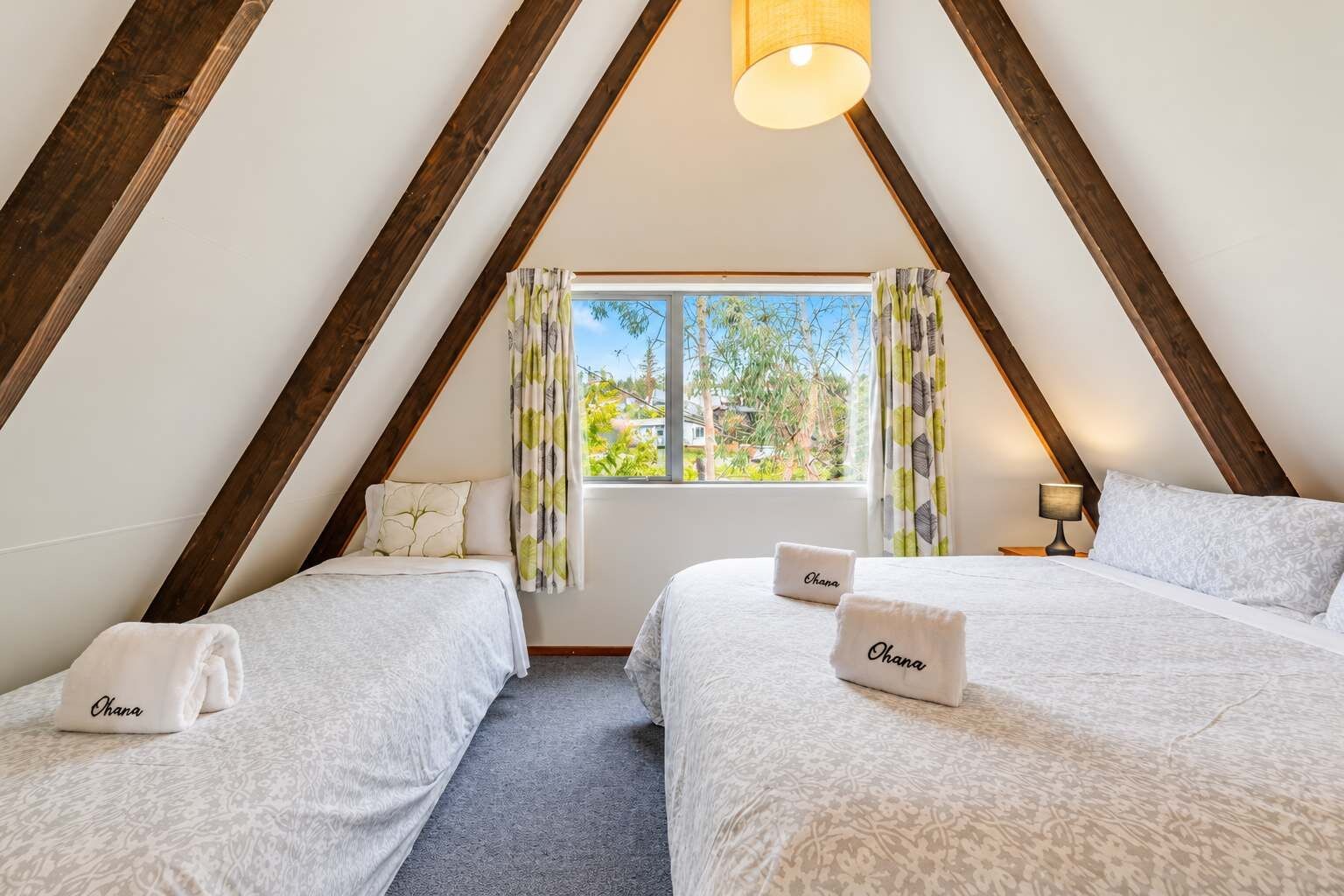 A room with two beds, a window with curtains, a lamp, and a ceiling light.