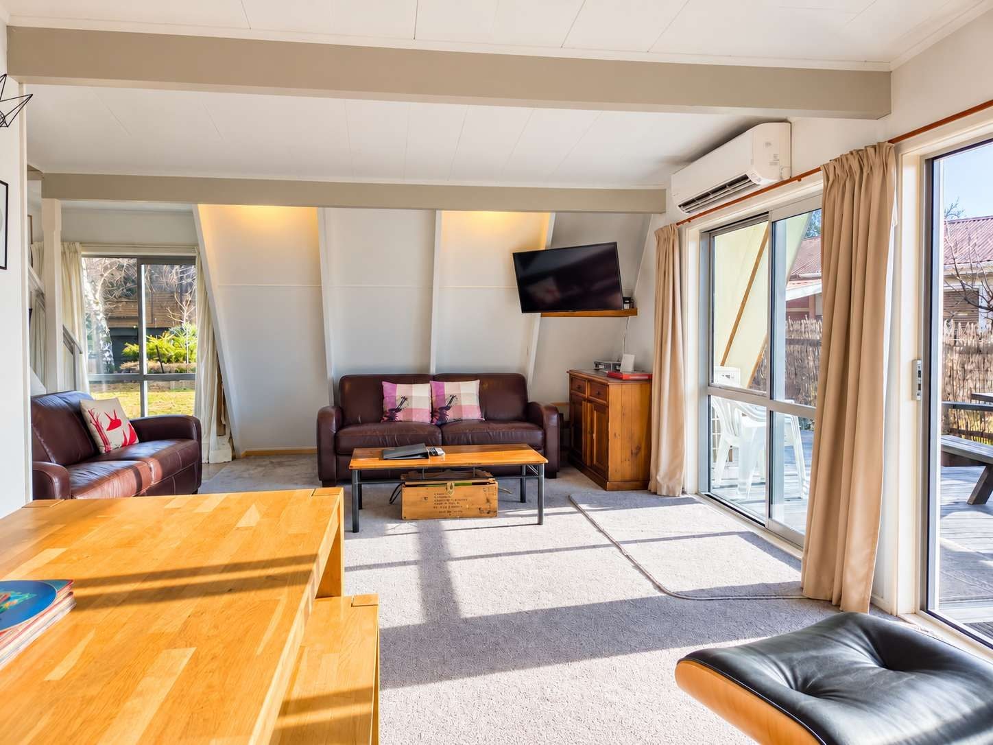 A living room with a sofa, a wooden coffee table, a television mounted on the wall, and a large window with curtains.