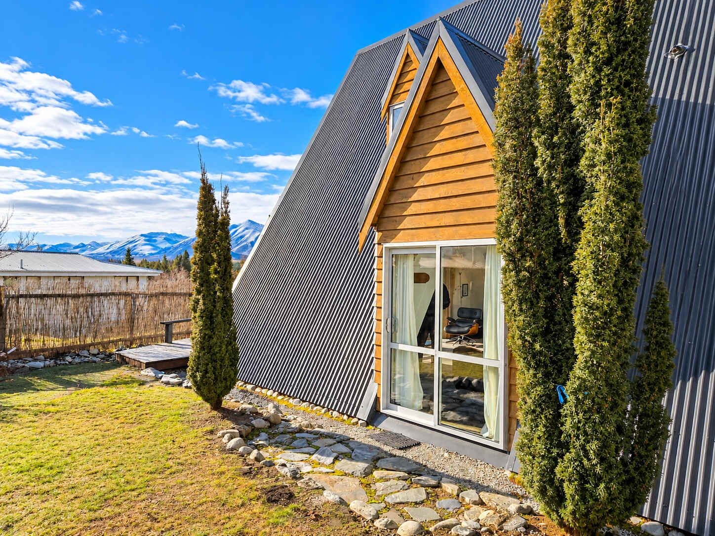 A modern house with a sloped roof, a large window, and a stone pathway leading to the entrance.