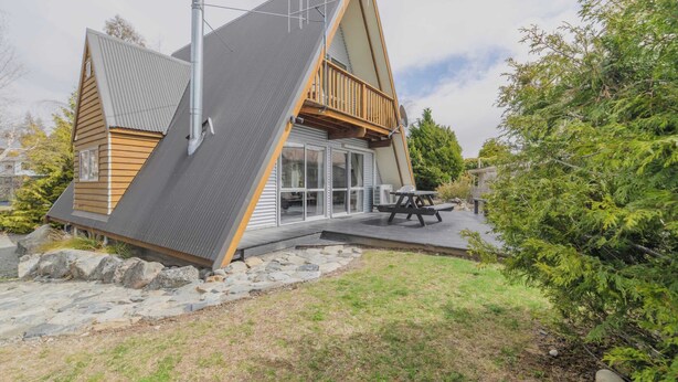 Una casa moderna tipo cabaña con base de piedra, una terraza grande y una mesa de picnic.