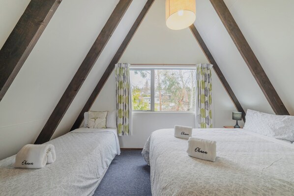 Una habitación con dos camas, cada una con una almohada que dice 'Ohana'. Hay una ventana con cortinas, una lámpara en una mesita de noche y una lámpara colgante en el techo.