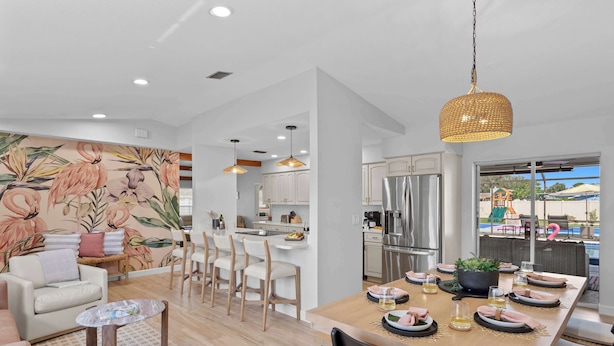 A modern kitchen with white cabinets, a stainless steel refrigerator, and a dining area with a wooden table set for six.