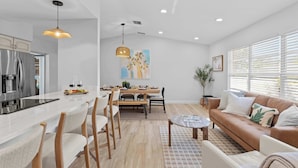 A modern kitchen with a central island, dining area with a wooden table and chairs, and a living area with a sofa and coffee table.
