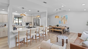 A modern kitchen with white cabinets, a central island with bar stools, and a dining area with a wooden table and chairs.