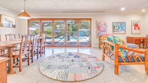 Un amplio salón con un gran ventanal que da a una piscina, un tapete circular de mosaico y muebles de madera.
