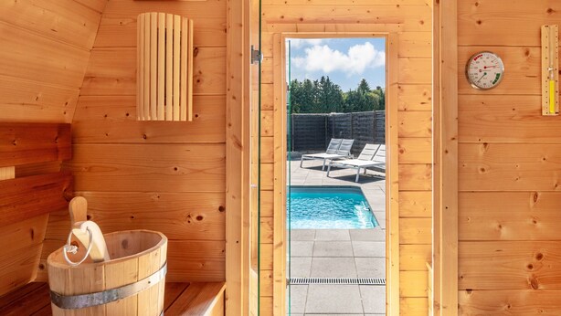 A wooden sauna room with a wooden bucket, a thermometer, and a view of an outdoor swimming pool. - Holiday Home 'Fewo Neubörger Wellness' with Private Pool, Wi-Fi and Air Conditioning (Neubörger)