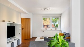 A modern living room with a flat-screen TV, grey sofas, a coffee table, and a large window with a view of a building. - Holiday Home 'Fewo Neubörger Wellness' with Private Pool, Wi-Fi and Air Conditioning (Neubörger)