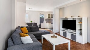 A modern living room with a grey sectional sofa, a white coffee table, and a large flat-screen TV on a white entertainment unit. - Holiday Home 'Fewo Neubörger Wellness' with Private Pool, Wi-Fi and Air Conditioning (Neubörger)