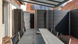 An outdoor patio with a long table and chairs, a metal roof, and a view of a solar panel and a tiled roof in the background. - Holiday Home 'Fewo Neubörger Wellness' with Private Pool, Wi-Fi and Air Conditioning (Neubörger)