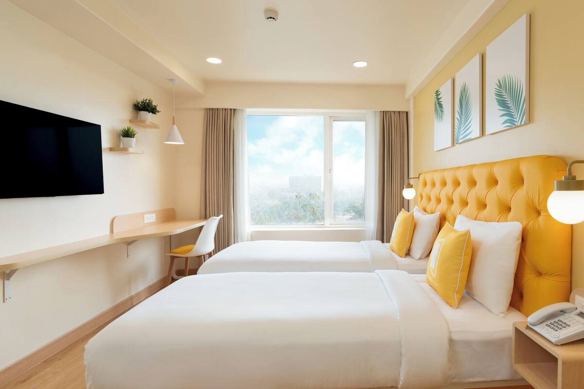 Habitación de hotel con dos camas, televisión, escritorio, silla, ventana con vistas y teléfono en la mesita de noche.