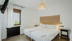 A bedroom with two beds, a window with curtains, a radiator, a woven headboard, a bedside table, and a hanging light fixture. - Country House in Torrecaballeros with Mountain Views, Private Pool, and Wi-Fi (Torrecaballeros)