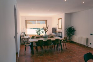 Ein Essbereich mit Tisch und Stühlen, einer Couch, einem Heizkörper und einem Fenster mit Jalousien.